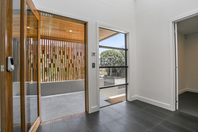 Large contemporary front door in Brisbane with beige walls, porcelain floors, a pivot front door, a light wood front door and black floor.