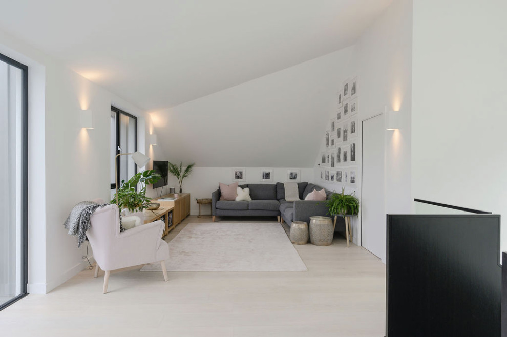 Modelo de salón abierto y abovedado actual grande con paredes blancas, suelo de madera clara y televisor colgado en la pared