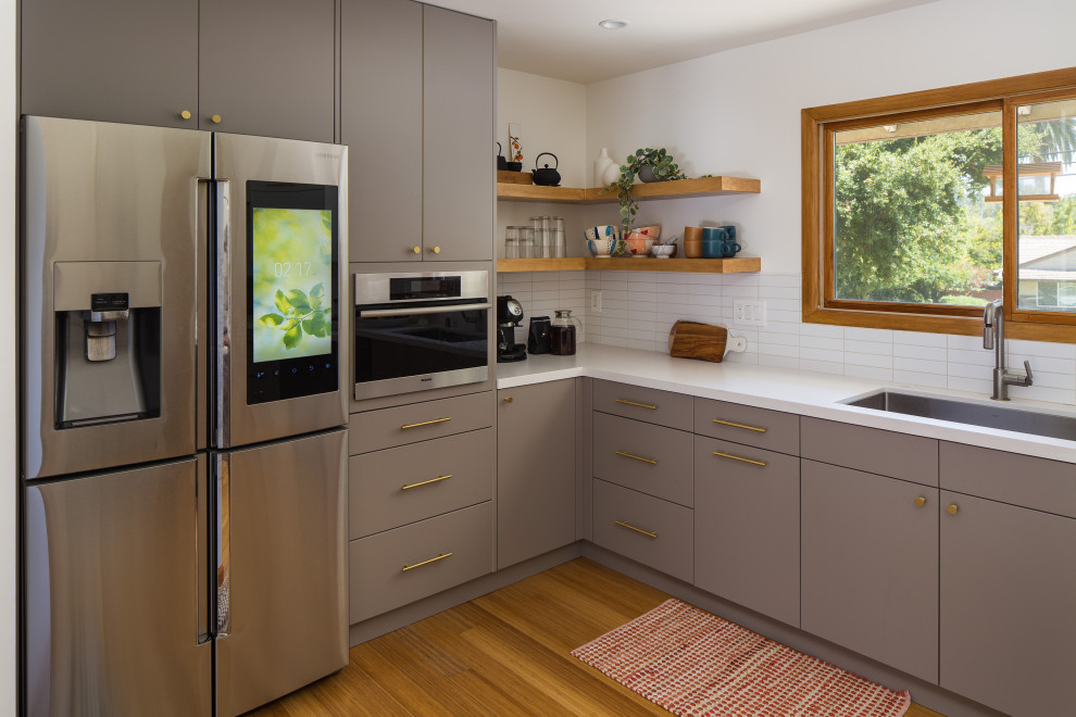 Photo of an expansive scandinavian galley eat-in kitchen in Los Angeles with an undermount sink, flat-panel cabinets, grey cabinets, quartz benchtops, white splashback, subway tile splashback, stainless steel appliances, bamboo floors, a peninsula, yellow floor and white benchtop.