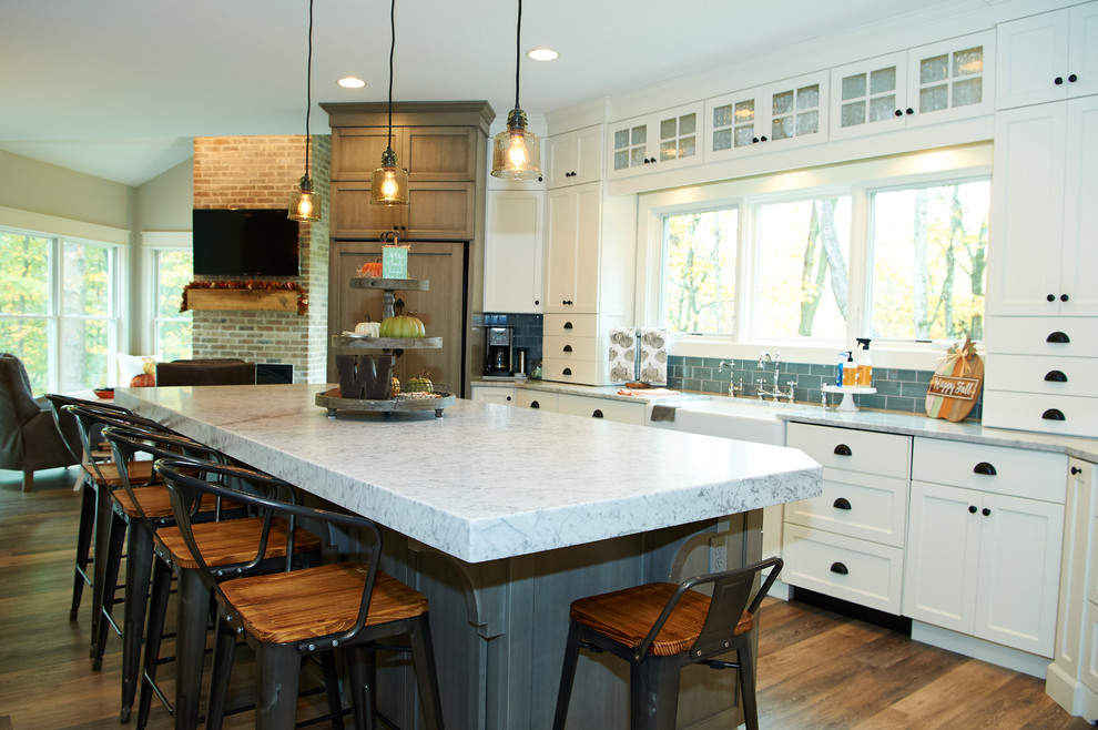 Inspiration for a large country u-shaped eat-in kitchen in Indianapolis with a farmhouse sink, shaker cabinets, white cabinets, marble benchtops, grey splashback, glass tile splashback, stainless steel appliances, vinyl floors, with island and brown floor.