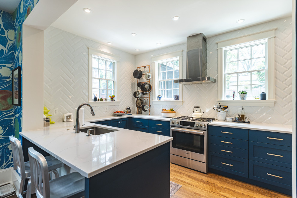 Inspiration for a mid-sized eclectic u-shaped eat-in kitchen in DC Metro with shaker cabinets, blue cabinets, quartz benchtops, white splashback, subway tile splashback, stainless steel appliances, light hardwood floors, a peninsula, brown floor and white benchtop.