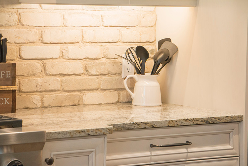 Example of a large transitional l-shaped home design design with a double-bowl sink, shaker cabinets, white cabinets, beige backsplash, stainless steel appliances and an island