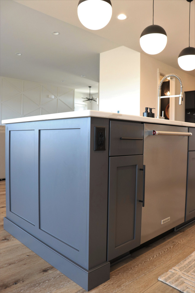 Large transitional l-shaped medium tone wood floor and brown floor open concept kitchen photo with a single-bowl sink, shaker cabinets, white cabinets, quartz countertops, gray backsplash, subway tile backsplash, stainless steel appliances, an island and white countertops