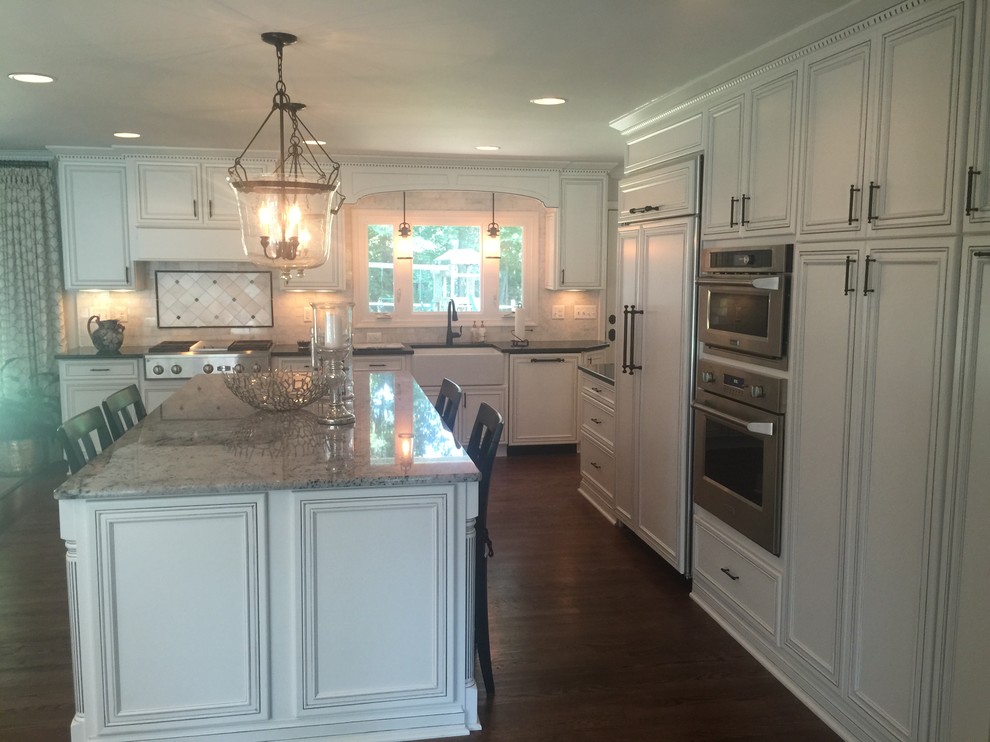 Inspiration for a large transitional l-shaped dark wood floor eat-in kitchen remodel in Baltimore with a farmhouse sink, flat-panel cabinets, white cabinets, granite countertops, white backsplash, stone tile backsplash, paneled appliances and an island