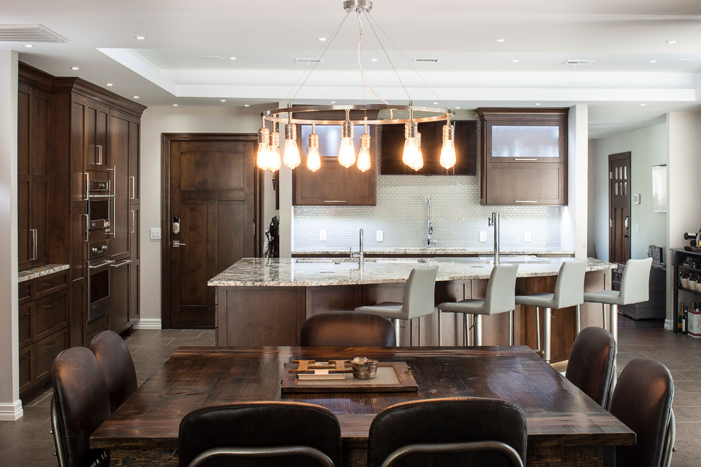 Eat-in kitchen - large transitional ceramic tile and beige floor eat-in kitchen idea with an undermount sink, shaker cabinets, brown cabinets, granite countertops, white backsplash, glass tile backsplash, stainless steel appliances and an island