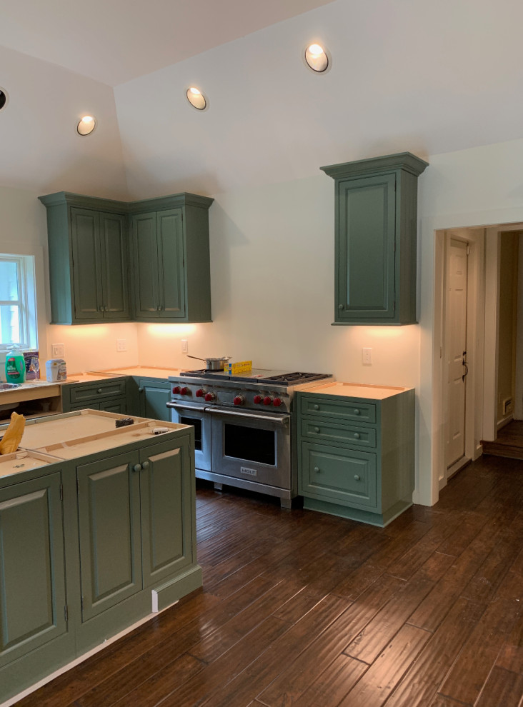 Example of a transitional u-shaped kitchen design with a farmhouse sink, raised-panel cabinets, green cabinets, soapstone countertops, stainless steel appliances and an island