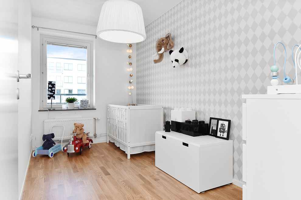 Photo of a mid-sized transitional gender-neutral nursery in Stockholm with white walls, medium hardwood floors and beige floor.