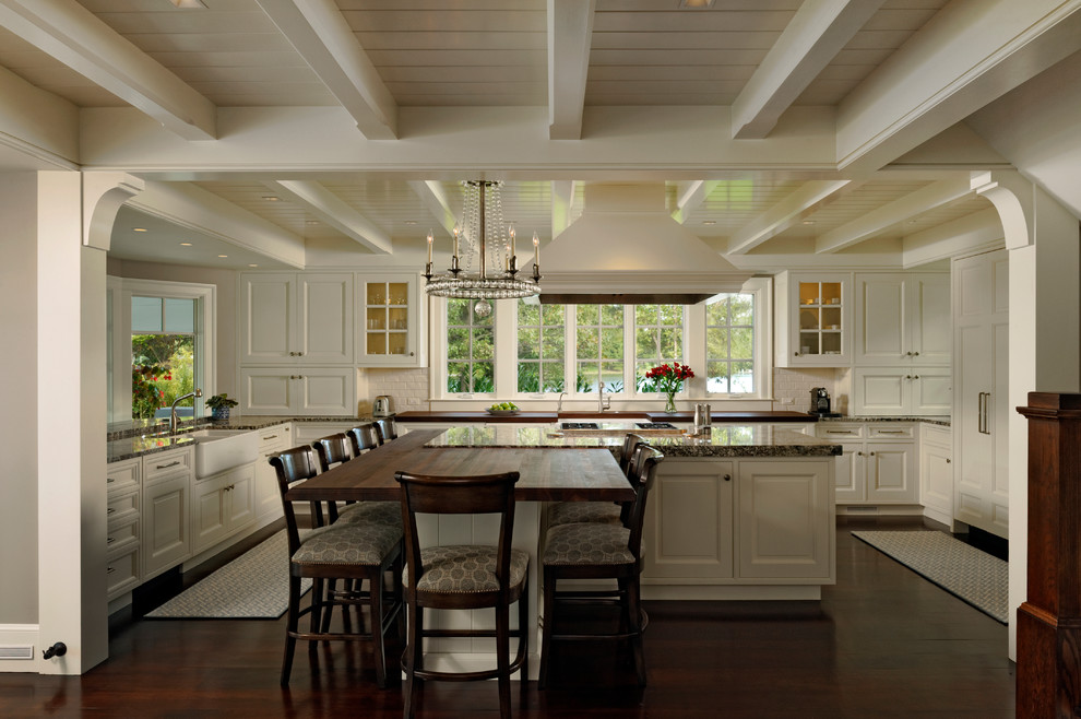 Inspiration for a large traditional u-shaped eat-in kitchen in Baltimore with white cabinets, granite benchtops, white splashback, subway tile splashback, dark hardwood floors, with island, panelled appliances, a farmhouse sink and raised-panel cabinets.