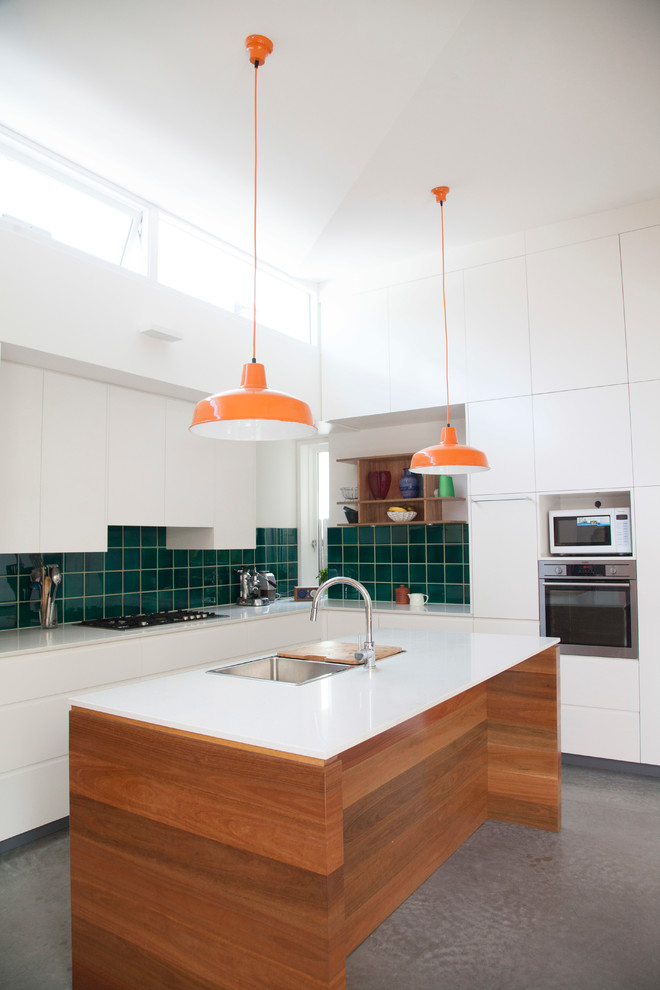 Contemporary l-shaped kitchen in Sydney with with island, flat-panel cabinets, white cabinets, green splashback and concrete floors.
