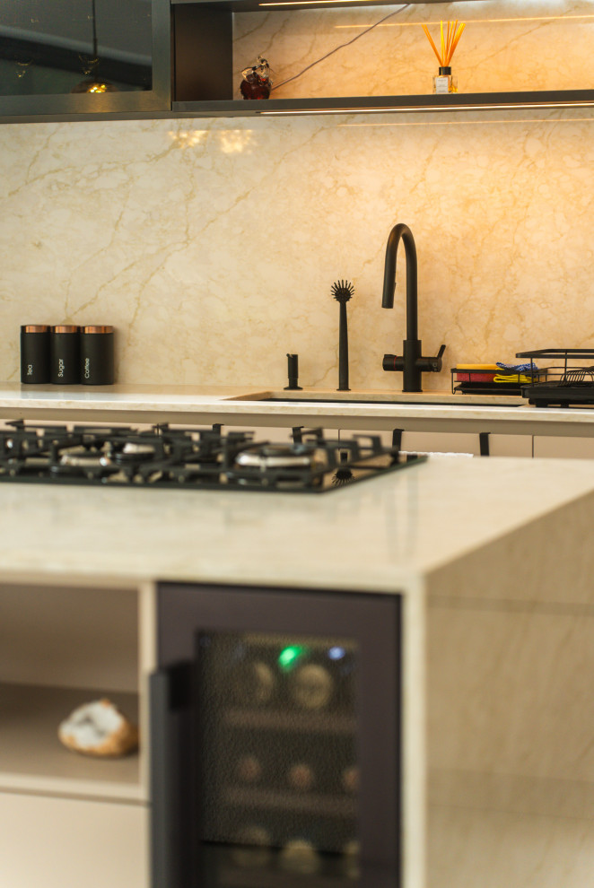 Inspiration for a medium sized cream and black single-wall open plan kitchen in London with beige cabinets, quartz worktops, beige splashback, engineered quartz splashback, black appliances, porcelain flooring, an island, grey floors, beige worktops and feature lighting.