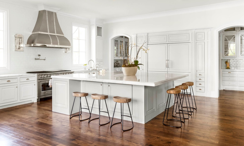 Open concept kitchen - huge traditional l-shaped medium tone wood floor open concept kitchen idea in Dallas with raised-panel cabinets, white cabinets, marble countertops, white backsplash, ceramic backsplash, paneled appliances, an island and a farmhouse sink