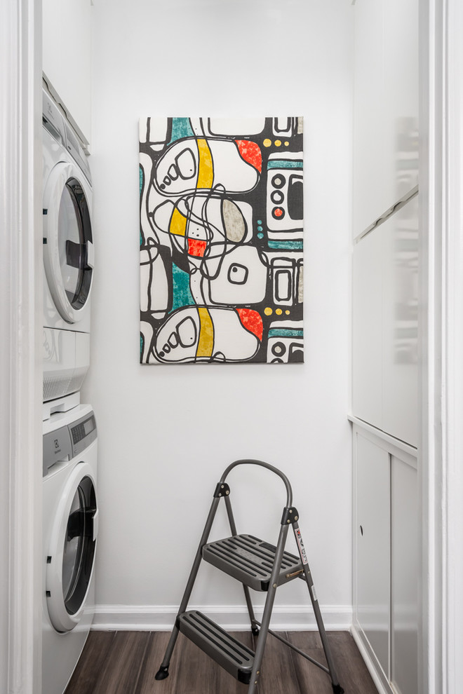 Photo of a small contemporary galley laundry cupboard in Atlanta with flat-panel cabinets, white cabinets, bamboo floors, grey floor, white walls and a stacked washer and dryer.
