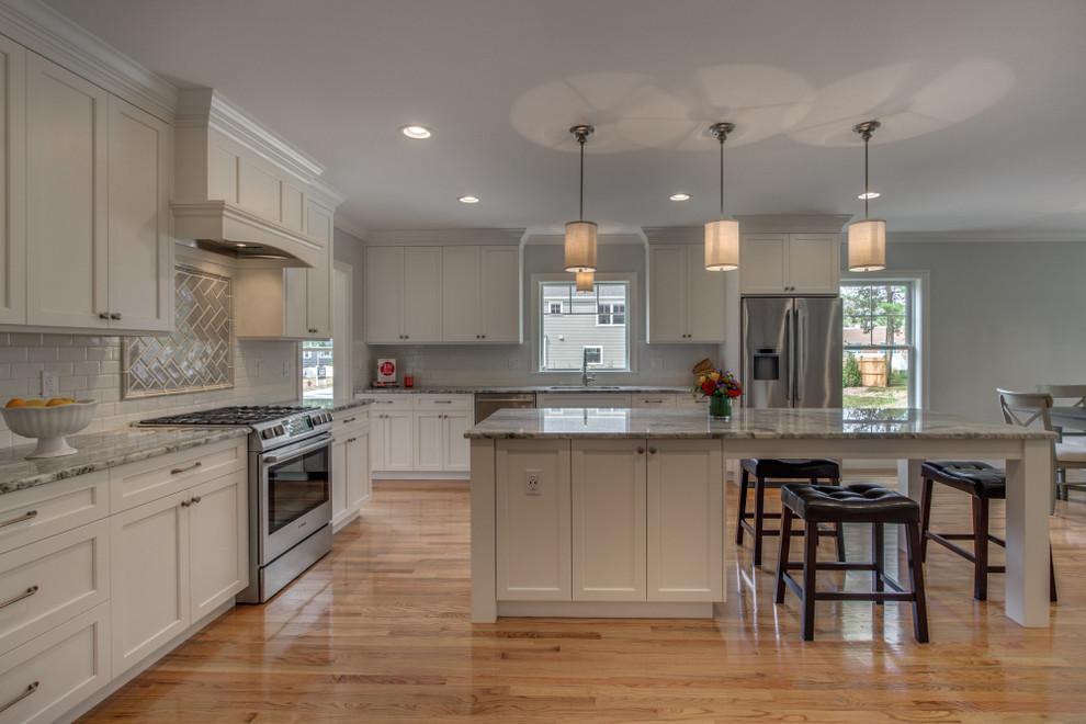 Inspiration for a large transitional single-wall eat-in kitchen in Boston with an undermount sink, white cabinets, granite benchtops, white splashback, subway tile splashback, stainless steel appliances, medium hardwood floors, with island, shaker cabinets and brown floor.