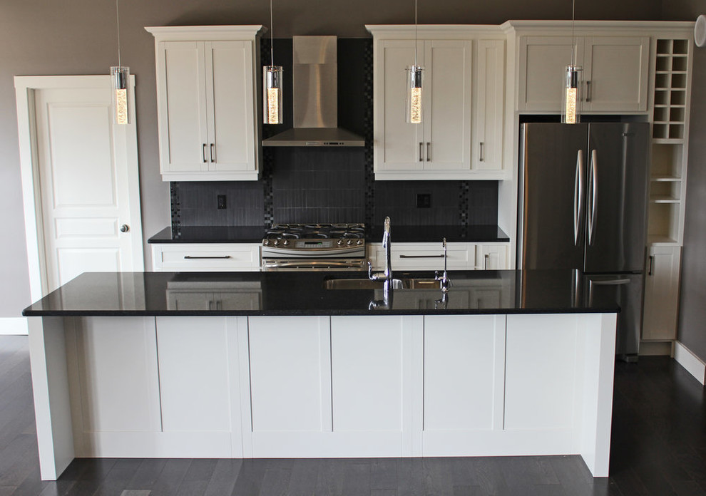 Mid-sized transitional galley open concept kitchen photo with a double-bowl sink, shaker cabinets, white cabinets, quartz countertops, gray backsplash, porcelain backsplash, stainless steel appliances, an island and black countertops