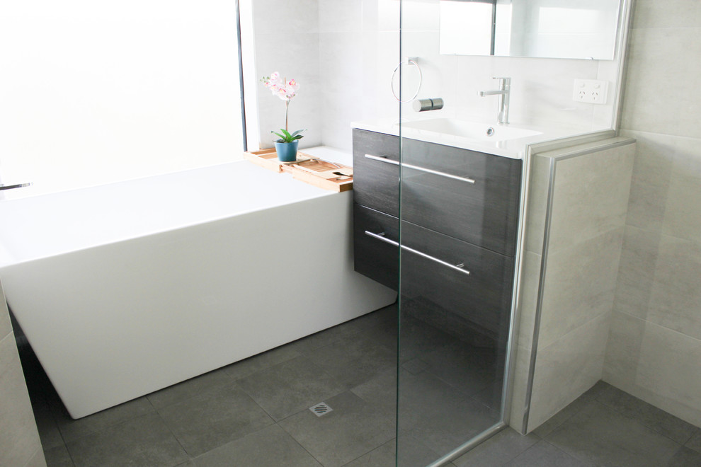 This is an example of a small kids bathroom in Perth with flat-panel cabinets, dark wood cabinets, a freestanding tub, a corner shower, gray tile, porcelain tile, grey walls, porcelain floors, an integrated sink, solid surface benchtops, grey floor, a hinged shower door and white benchtops.