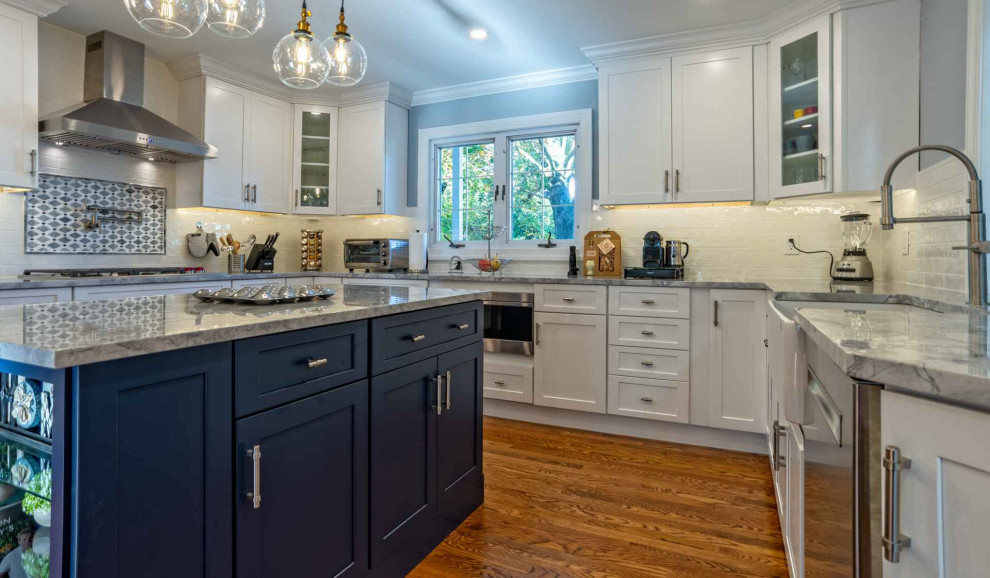 Inspiration for a mid-sized transitional u-shaped eat-in kitchen in Philadelphia with a farmhouse sink, shaker cabinets, blue cabinets, quartz benchtops, white splashback, porcelain splashback, stainless steel appliances, medium hardwood floors, with island, brown floor and grey benchtop.