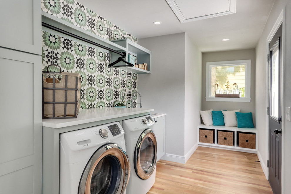 Inspiration for a transitional single-wall laundry room in Austin with an undermount sink, shaker cabinets, grey cabinets, grey walls, medium hardwood floors, a side-by-side washer and dryer, brown floor and white benchtop.