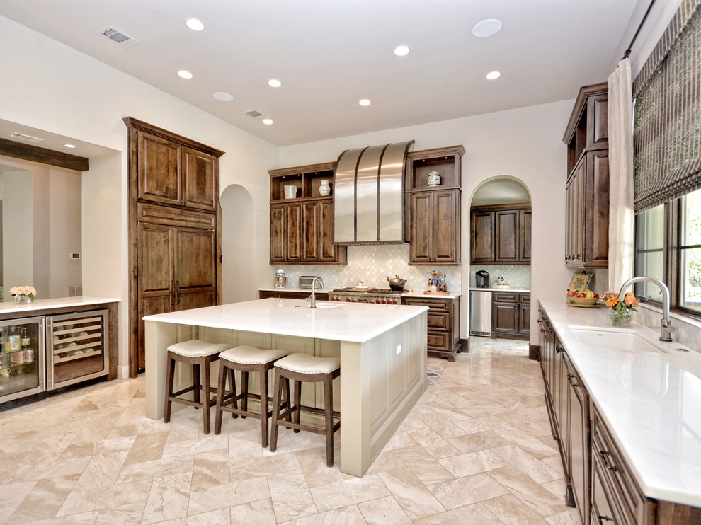 This is an example of a large transitional u-shaped open plan kitchen in Austin with a drop-in sink, raised-panel cabinets, medium wood cabinets, quartzite benchtops, white splashback, glass tile splashback, panelled appliances, travertine floors and with island.
