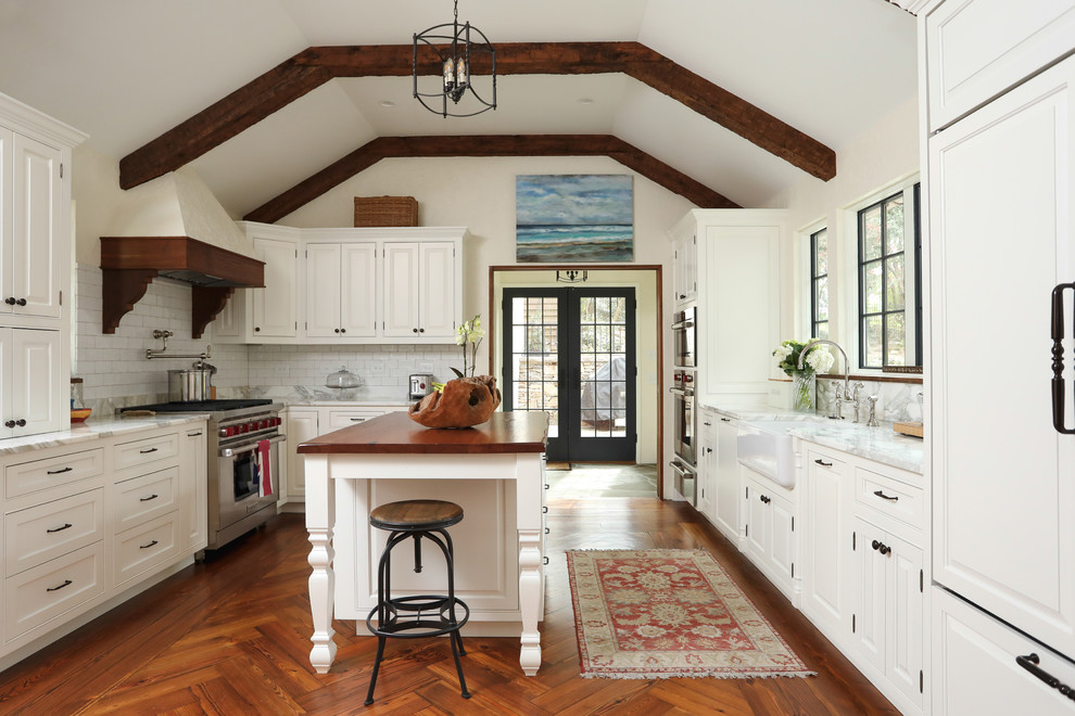 Photo of a traditional kitchen in Raleigh with a farmhouse sink, white cabinets, white splashback, subway tile splashback, medium hardwood floors, with island, white benchtop and panelled appliances.