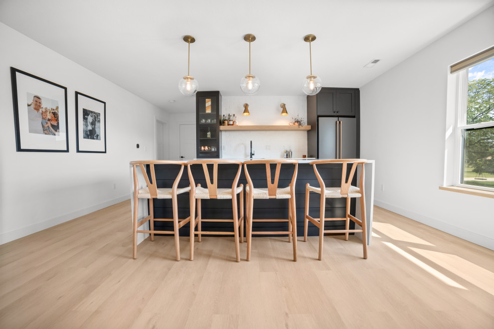 This is an example of a large scandinavian single-wall seated home bar in Cedar Rapids with a drop-in sink, beaded inset cabinets, dark wood cabinets, limestone benchtops, white splashback, vinyl floors, beige floor and white benchtop.
