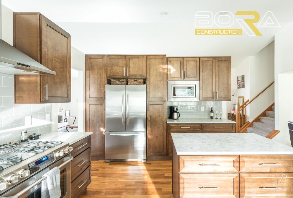 Eat-in kitchen - mid-sized transitional l-shaped medium tone wood floor and brown floor eat-in kitchen idea with an undermount sink, shaker cabinets, medium tone wood cabinets, quartz countertops, gray backsplash, ceramic backsplash, stainless steel appliances and an island