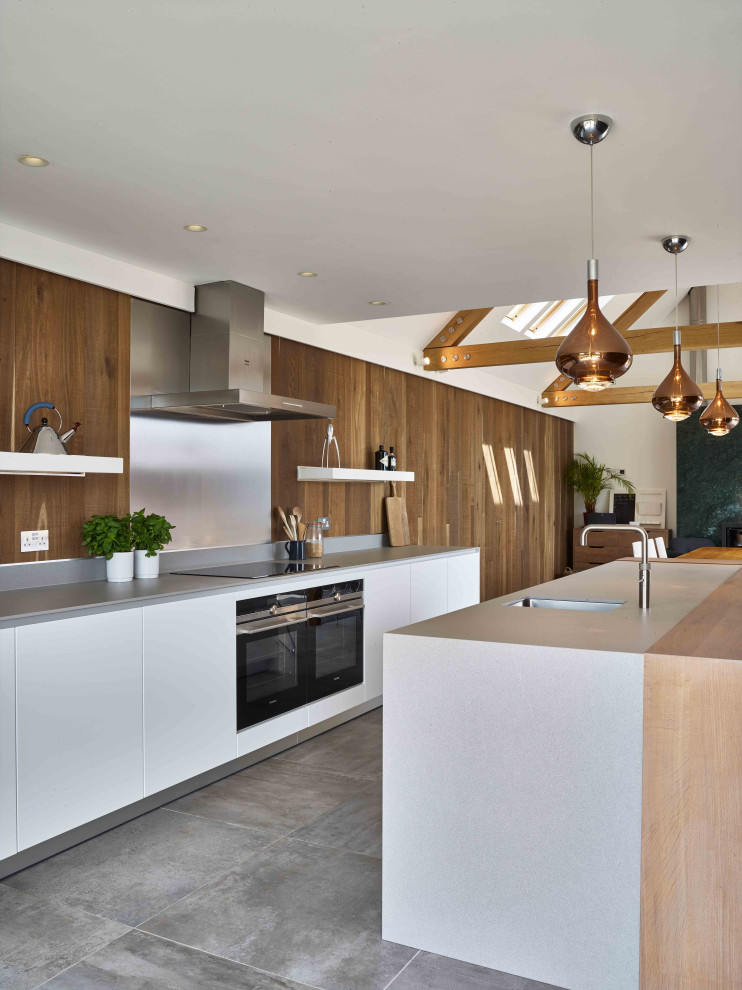 Photo of a large contemporary galley kitchen in Devon with an integrated sink, flat-panel cabinets, white cabinets, solid surface benchtops, timber splashback, ceramic floors, with island, grey floor and grey benchtop.
