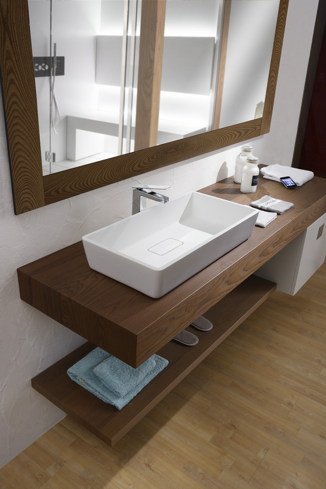 This is an example of a modern bathroom in London with a wall-mount sink, furniture-like cabinets, medium wood cabinets, wood benchtops and white walls.