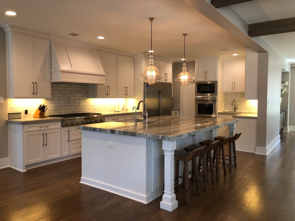 Inspiration for a large transitional l-shaped medium tone wood floor and brown floor open concept kitchen remodel in Dallas with an undermount sink, shaker cabinets, white cabinets, quartz countertops, gray backsplash, ceramic backsplash, stainless steel appliances and an island