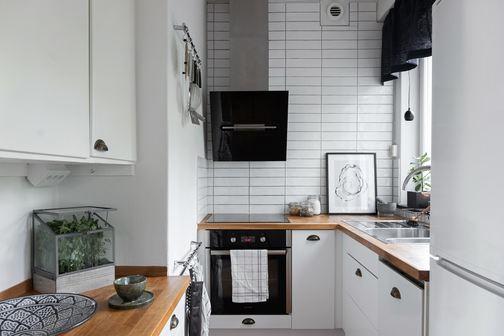Photo of a small scandinavian kitchen in Stockholm with a double-bowl sink, flat-panel cabinets, wood benchtops, white splashback, black appliances and no island.