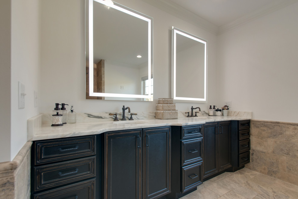 Photo of a mid-sized country master bathroom in Nashville with recessed-panel cabinets, black cabinets, a freestanding tub, an open shower, a one-piece toilet, white tile, ceramic tile, white walls, limestone floors, an undermount sink, marble benchtops, brown floor, an open shower, white benchtops, a double vanity and a built-in vanity.