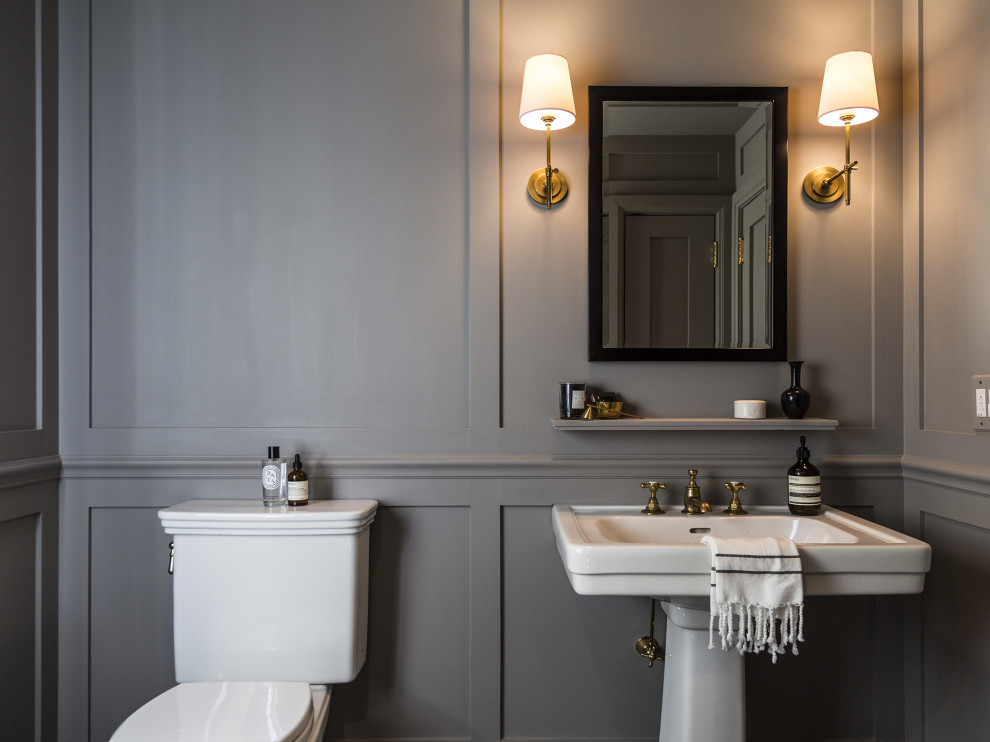 This is an example of a transitional powder room in New York with white cabinets, a two-piece toilet, grey walls, a pedestal sink, a built-in vanity and panelled walls.