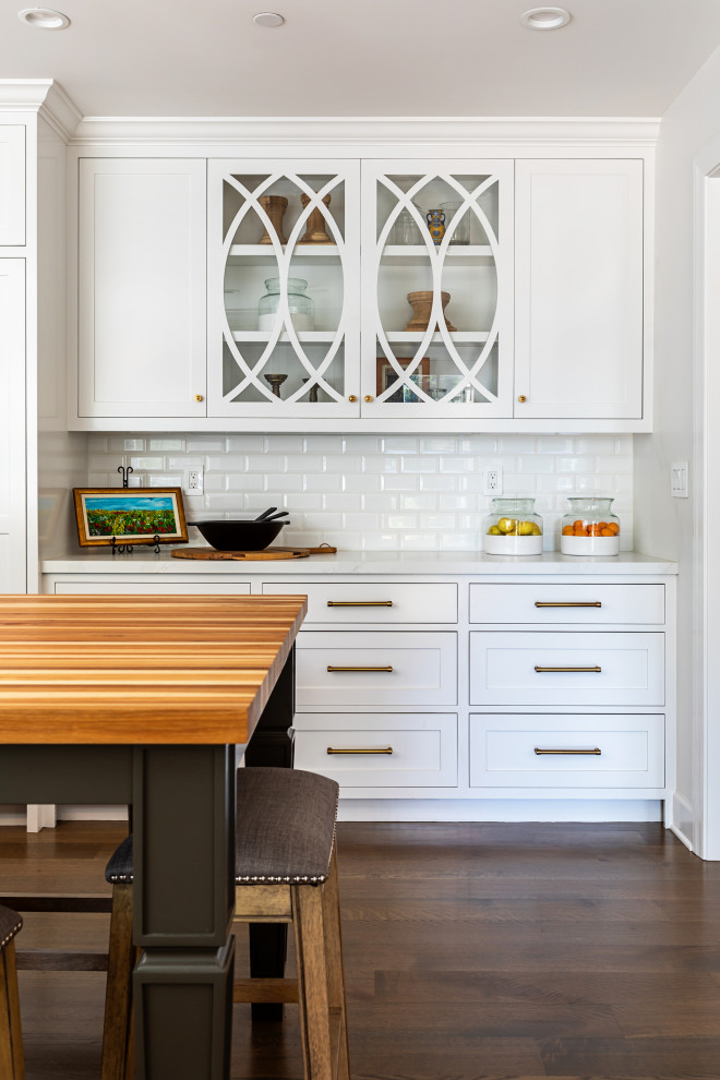 This is an example of a mid-sized country l-shaped separate kitchen in Los Angeles with a farmhouse sink, shaker cabinets, white cabinets, quartz benchtops, white splashback, subway tile splashback, stainless steel appliances, medium hardwood floors, with island, brown floor and white benchtop.