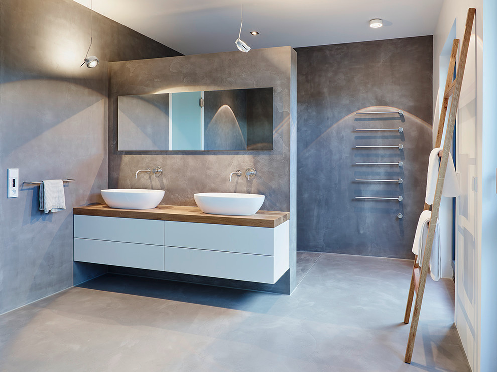 This is an example of a large contemporary master bathroom in Frankfurt with flat-panel cabinets, white cabinets, grey walls, concrete floors, a vessel sink, wood benchtops, a curbless shower and brown benchtops.
