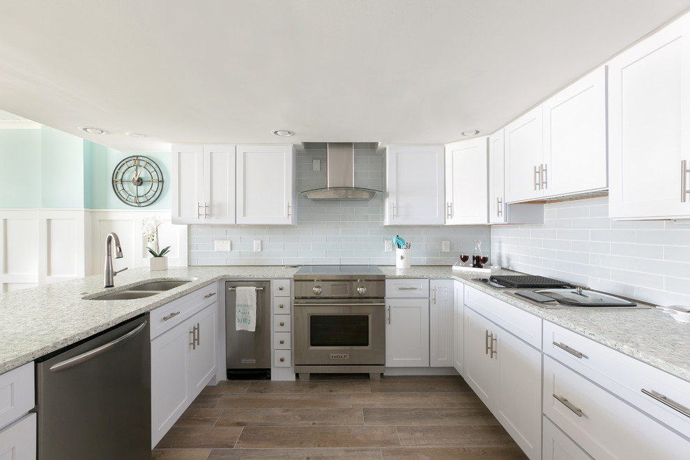 Photo of a large beach style u-shaped open plan kitchen in Charleston with an undermount sink, raised-panel cabinets, white cabinets, recycled glass benchtops, white splashback, subway tile splashback, stainless steel appliances, laminate floors, a peninsula and multi-coloured benchtop.