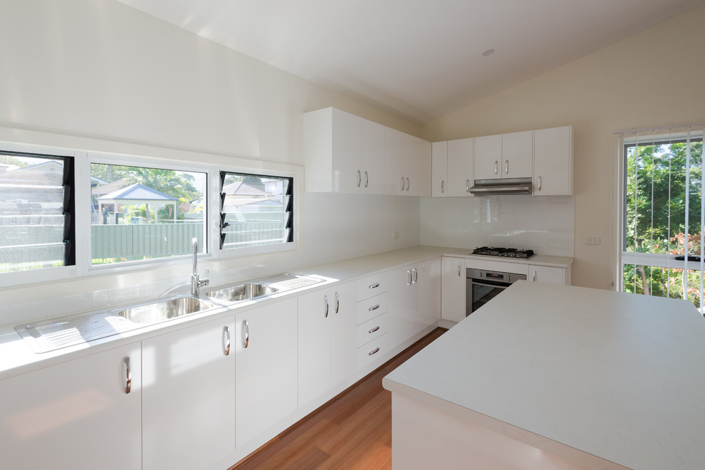 Design ideas for a mid-sized contemporary kitchen in Wollongong with a double-bowl sink, white cabinets, laminate benchtops, white splashback, ceramic splashback, stainless steel appliances and with island.