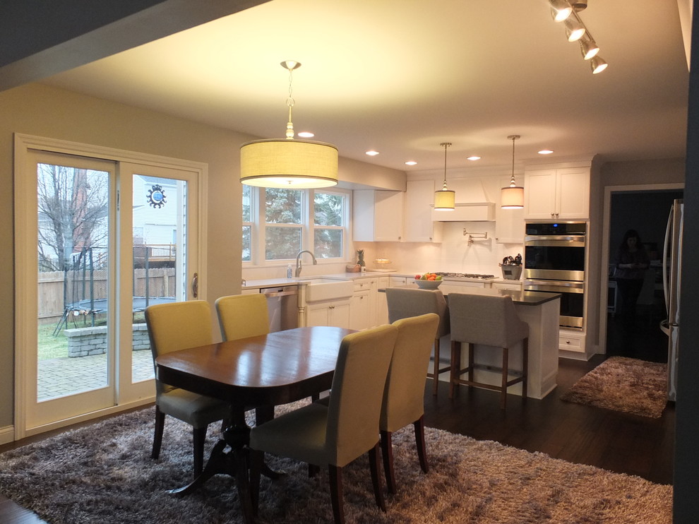 This is an example of a mid-sized transitional u-shaped eat-in kitchen in Columbus with with island, flat-panel cabinets, white cabinets, quartz benchtops, white splashback, ceramic splashback, stainless steel appliances, a farmhouse sink and dark hardwood floors.