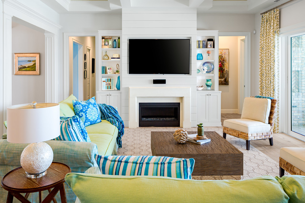 Design ideas for a mid-sized beach style open concept family room in Tampa with light hardwood floors, a standard fireplace, a stone fireplace surround, white walls, a wall-mounted tv and beige floor.