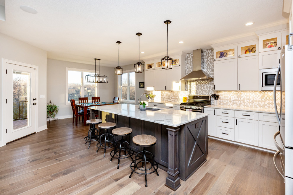 Open concept kitchen - large transitional l-shaped medium tone wood floor and brown floor open concept kitchen idea with an undermount sink, shaker cabinets, white cabinets, marble countertops, multicolored backsplash, ceramic backsplash, stainless steel appliances, an island and white countertops