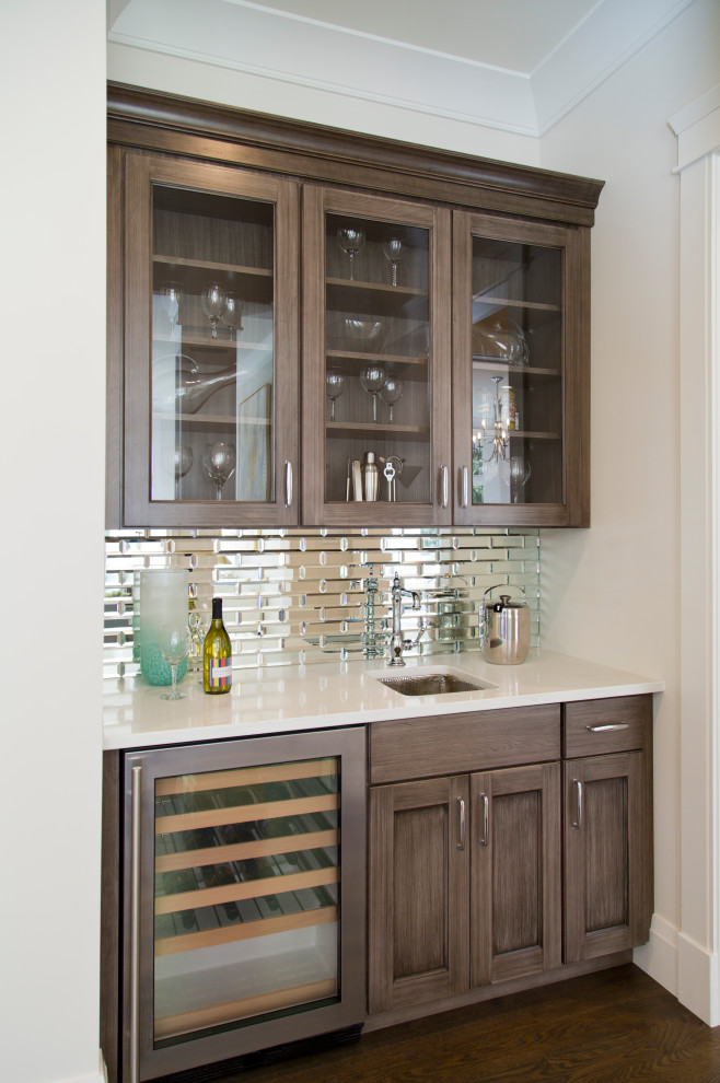 Small transitional single-wall wet bar in St Louis with an undermount sink, glass-front cabinets, marble benchtops, dark hardwood floors, brown floor, white benchtop, dark wood cabinets and metal splashback.