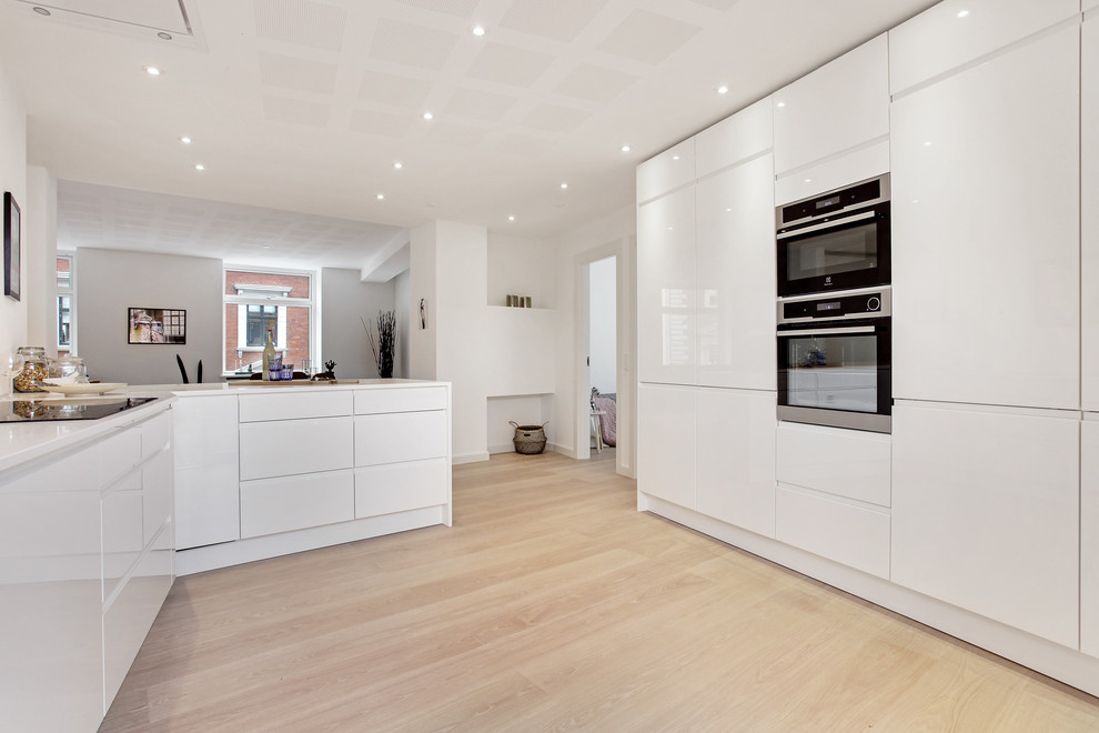 Modern u-shaped separate kitchen in Aarhus with an integrated sink, flat-panel cabinets, white cabinets, black appliances, light hardwood floors, with island and beige floor.