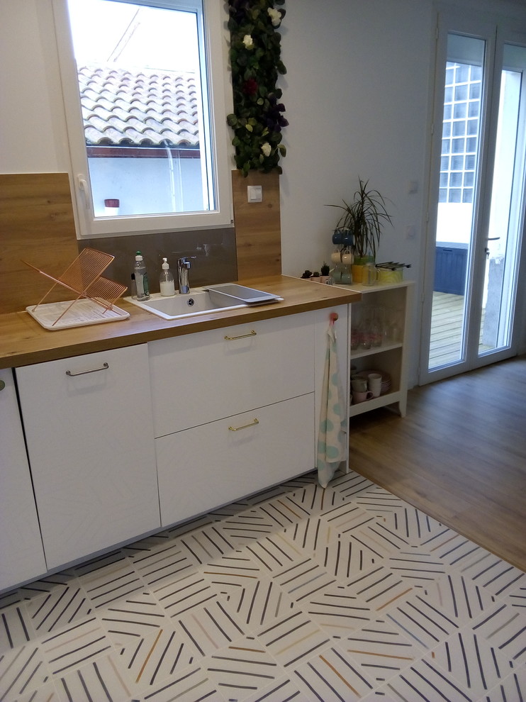 Small scandinavian l-shaped open plan kitchen in Montpellier with an undermount sink, beaded inset cabinets, white cabinets, wood benchtops, brown splashback, timber splashback, panelled appliances, cement tiles, no island, multi-coloured floor and brown benchtop.