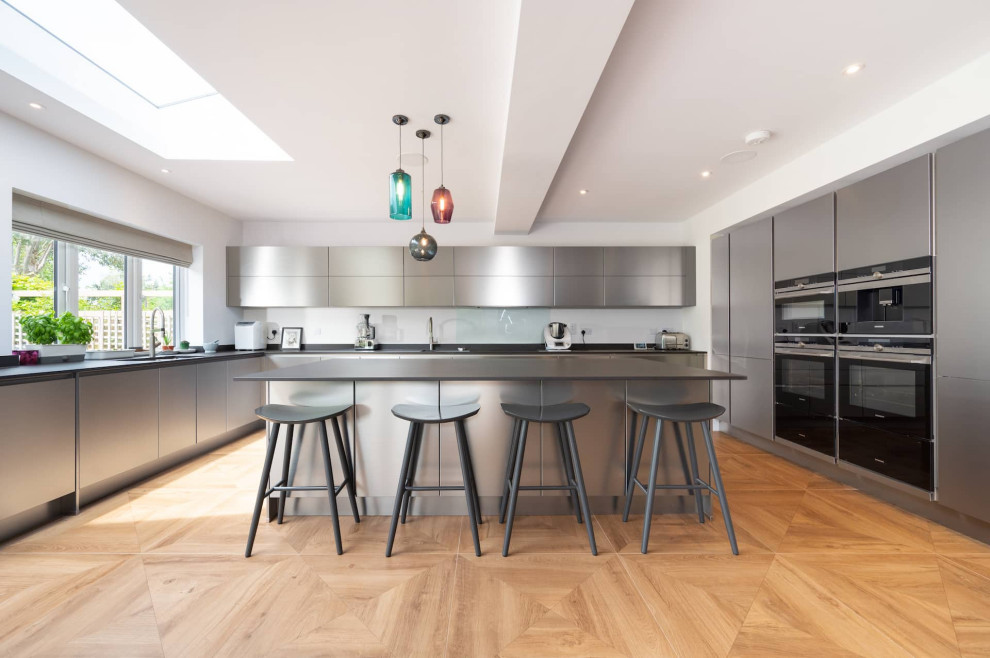 Design ideas for a large contemporary u-shaped open plan kitchen in Hertfordshire with a double-bowl sink, flat-panel cabinets, grey cabinets, stainless steel appliances, an island, grey worktops and feature lighting.