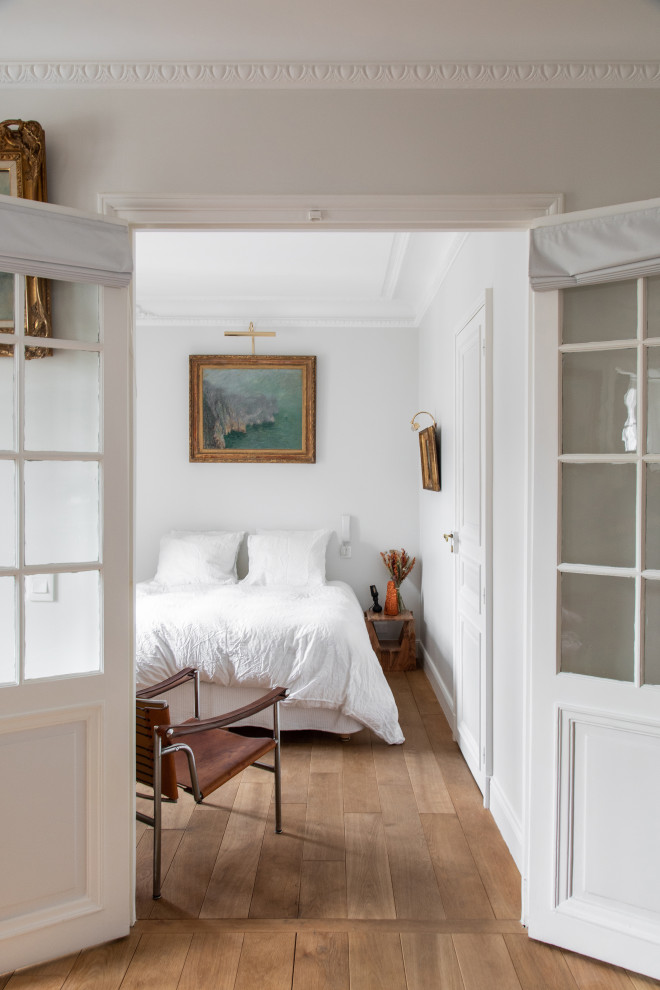 Aménagement d'une chambre parentale de taille moyenne avec un mur blanc, un sol en bois brun et aucune cheminée.