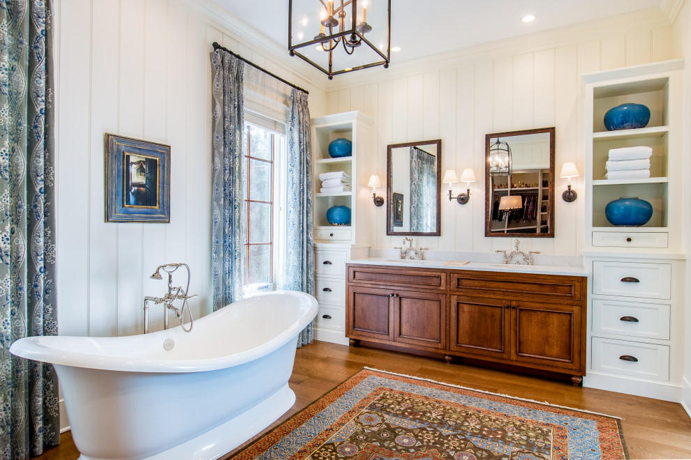 Design ideas for a large country master bathroom in Other with dark wood cabinets, a freestanding tub, white walls, medium hardwood floors, an undermount sink, marble benchtops, brown floor, white benchtops and recessed-panel cabinets.