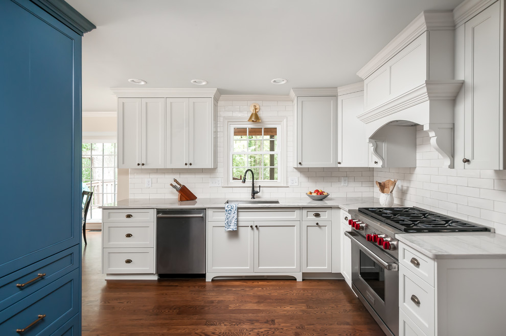 Example of a mid-sized transitional medium tone wood floor and brown floor kitchen design in Atlanta with shaker cabinets, white cabinets, white backsplash, stainless steel appliances, a farmhouse sink, quartzite countertops, ceramic backsplash, no island and white countertops