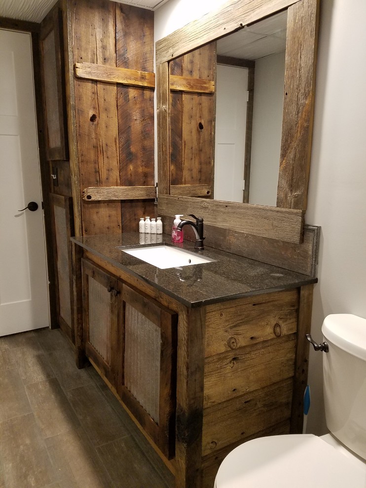 This is an example of a mid-sized country 3/4 bathroom in Minneapolis with louvered cabinets, dark wood cabinets, an alcove shower, a two-piece toilet, beige tile, stone tile, grey walls, medium hardwood floors, an undermount sink, engineered quartz benchtops, brown floor and a sliding shower screen.