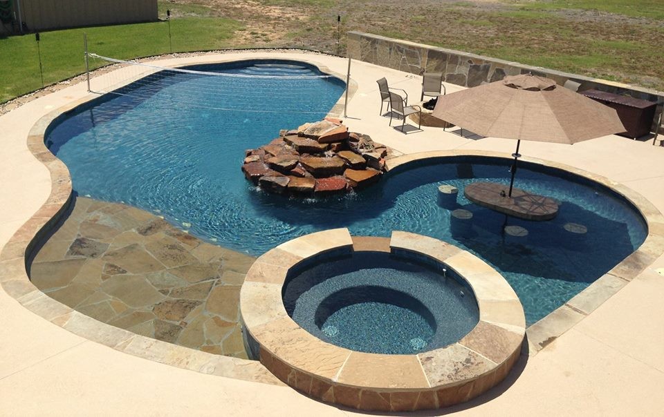 Large modern backyard custom-shaped natural pool in Houston with a hot tub and natural stone pavers.
