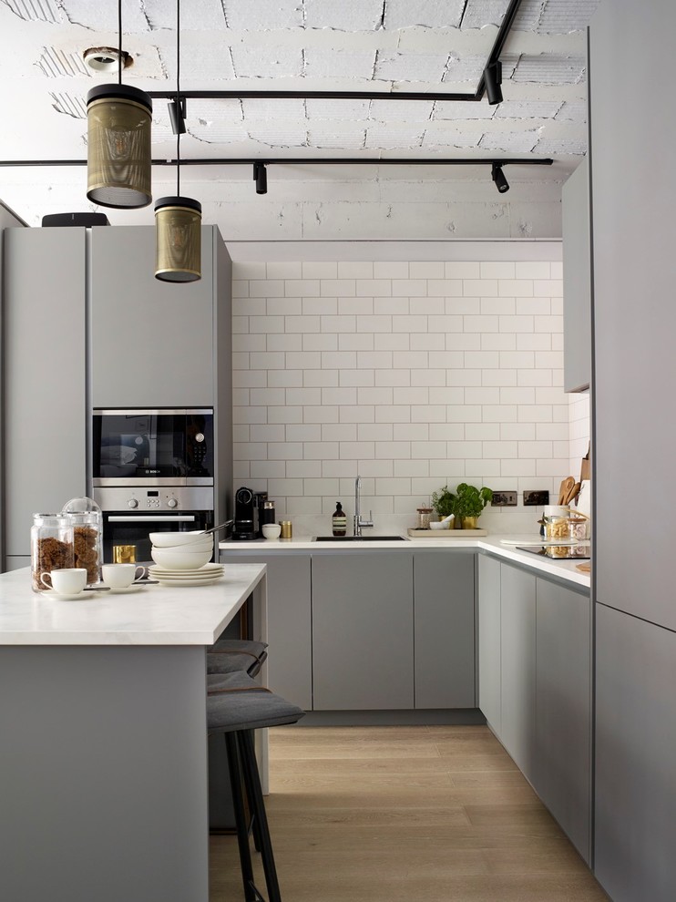 Inspiration for a contemporary l-shaped kitchen in London with a drop-in sink, flat-panel cabinets, grey cabinets, quartzite benchtops, stainless steel appliances, light hardwood floors, with island, beige floor, white benchtop, white splashback and subway tile splashback.