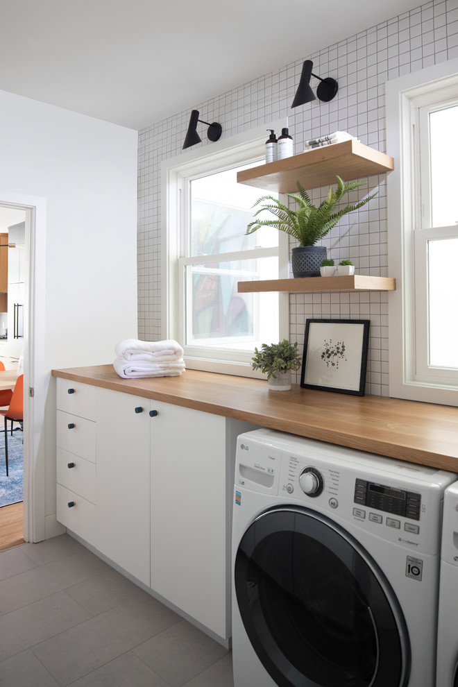 Example of a trendy gray floor dedicated laundry room design in San Francisco with flat-panel cabinets, white cabinets, wood countertops, white walls, a side-by-side washer/dryer and brown countertops