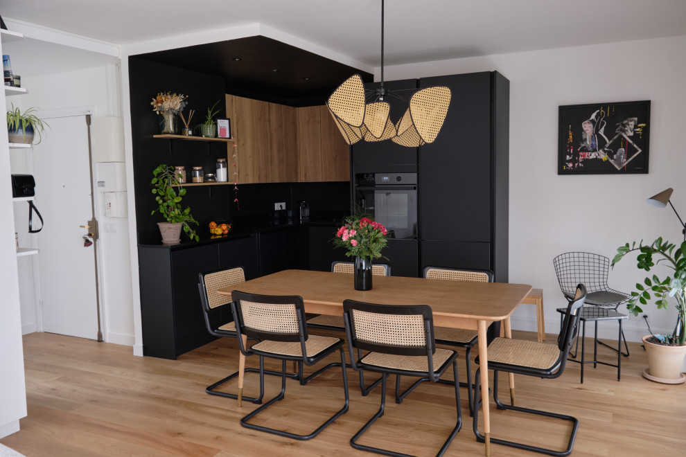 Cette image montre cuisine ouverte in L With un évier encastré, un placard à porte affleurante, des portes de placard noires, un plan de travail en granite, une crédence noire, parquet clair, aucun îlot, un sol beige and plan de travail noir.